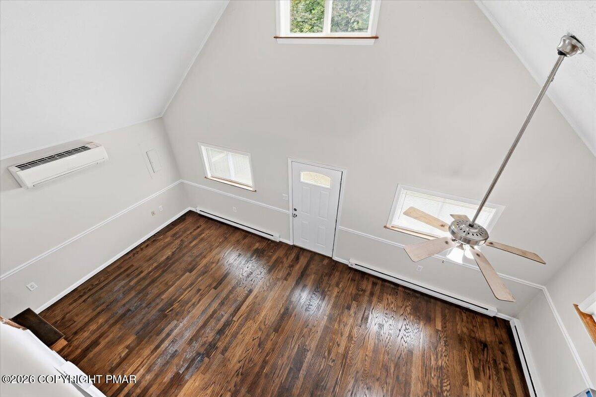 Vacant room with vaulted ceiling, dark hardwood floors, ceiling fan, and multiple windows.