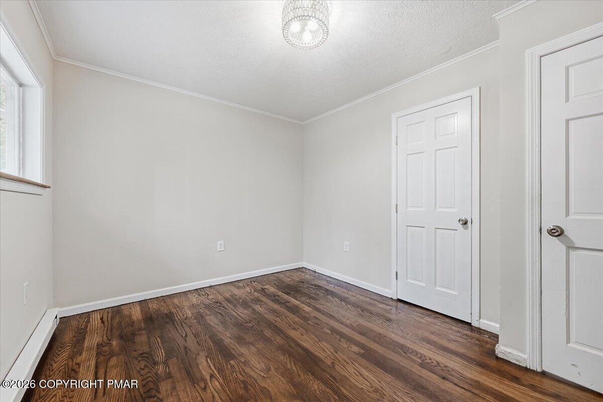 Vacant room with dark wood floors, a window, two white doors, and a ceiling light.