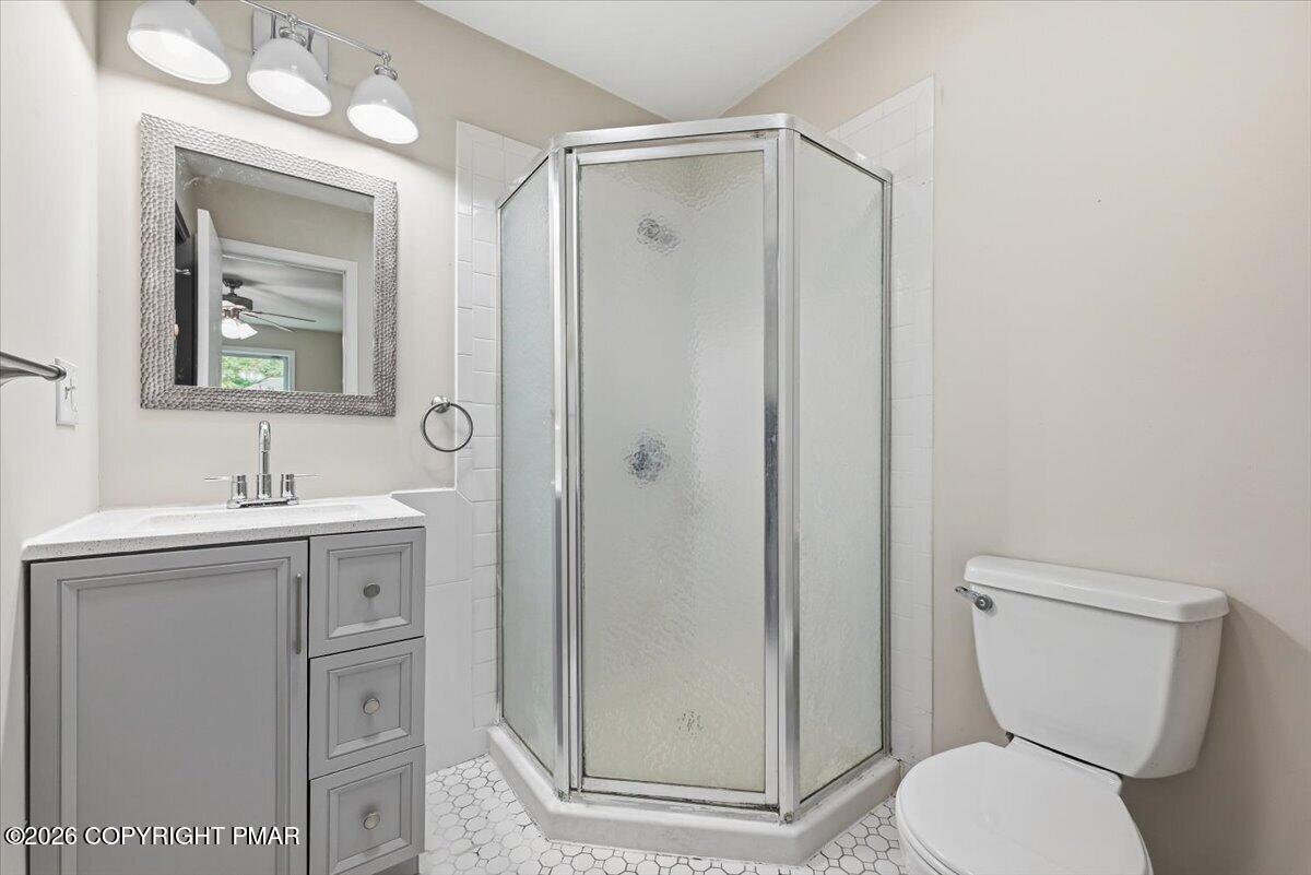 Bathroom with a gray vanity, framed mirror, corner glass shower, and white toilet.