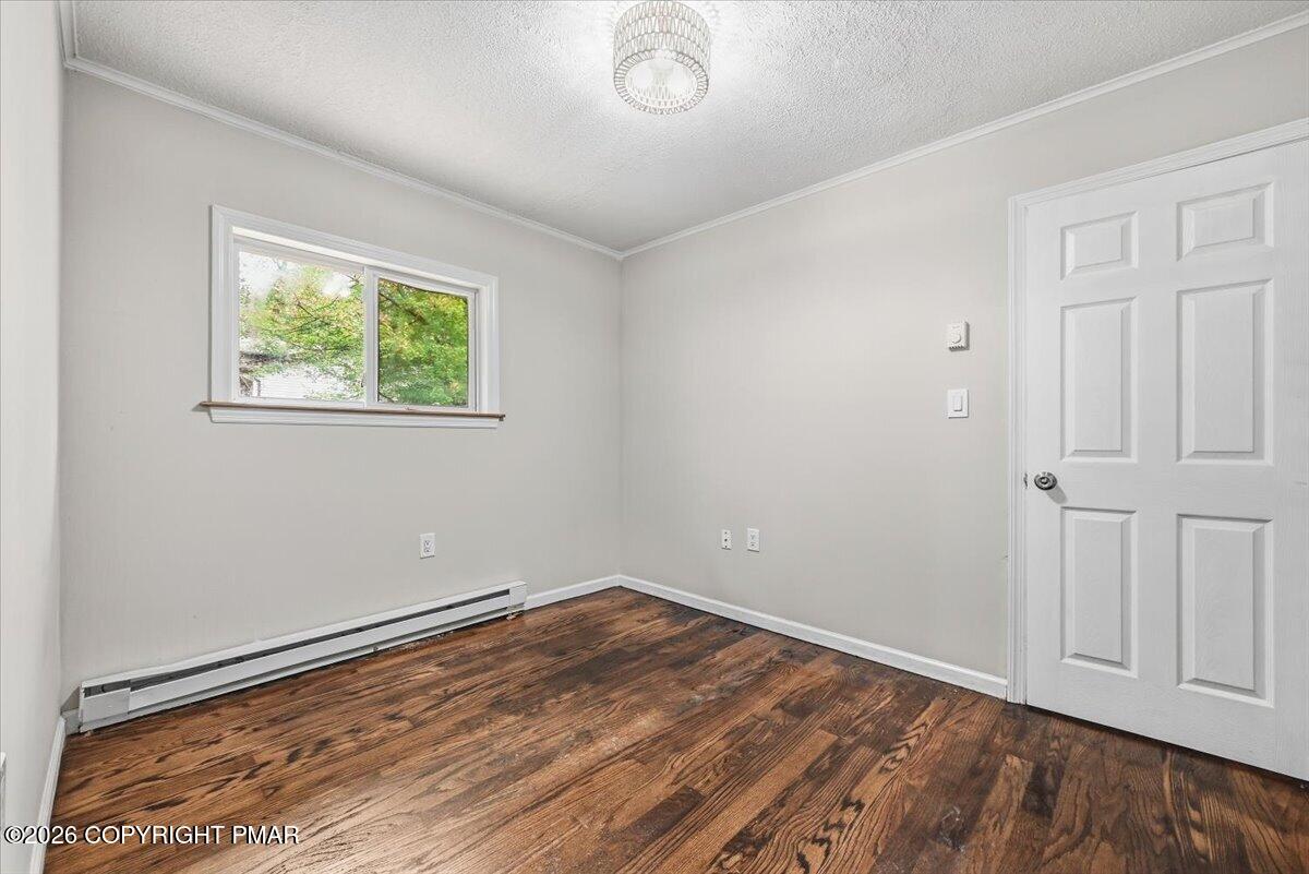 Empty room with dark wood flooring, a window, and a white paneled door.