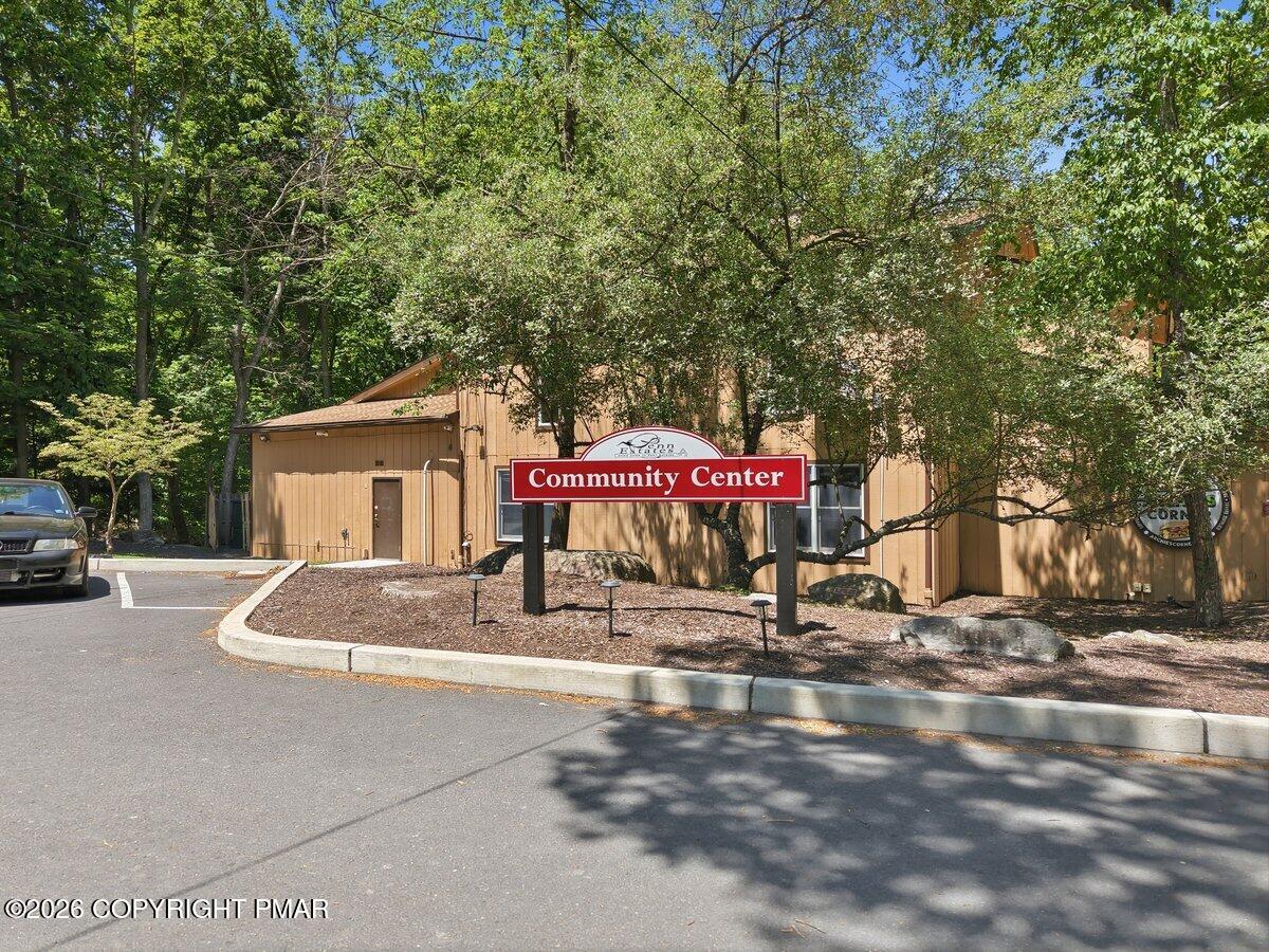 Community center among leafy trees, with a red sign and parking area in front.