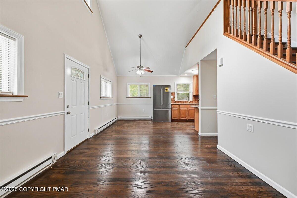 Unfurnished living and dining area with dark hardwood floors, vaulted ceiling, and adjoining kitchen.