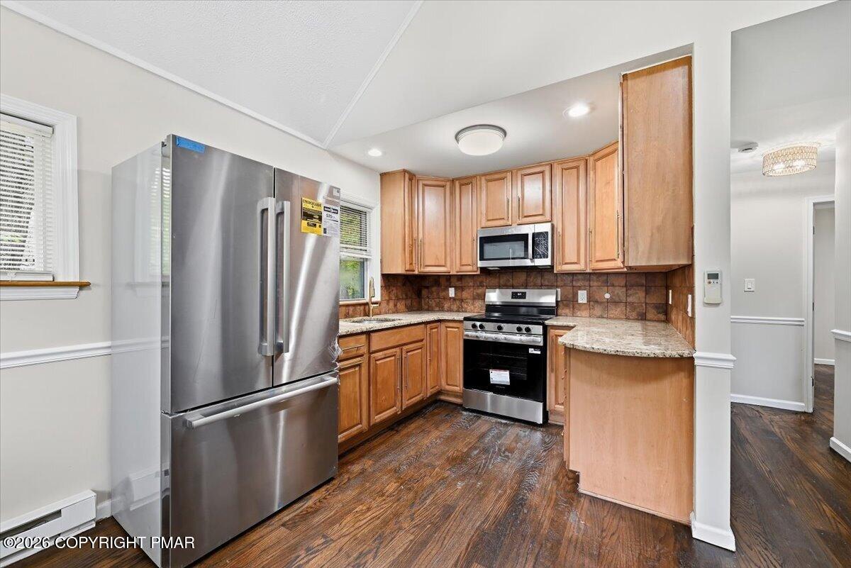 Kitchen with warm wood cabinets, stainless steel appliances, and dark wood flooring.
