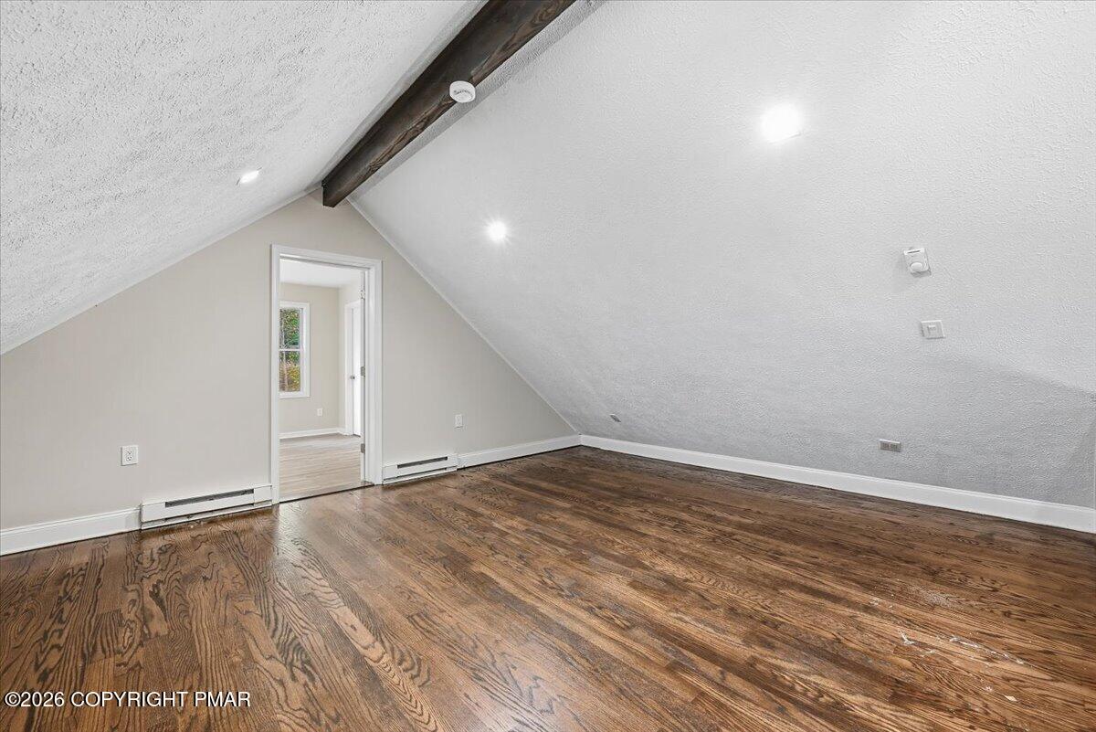 Empty attic room with sloped ceilings, an exposed beam, and hardwood floors.