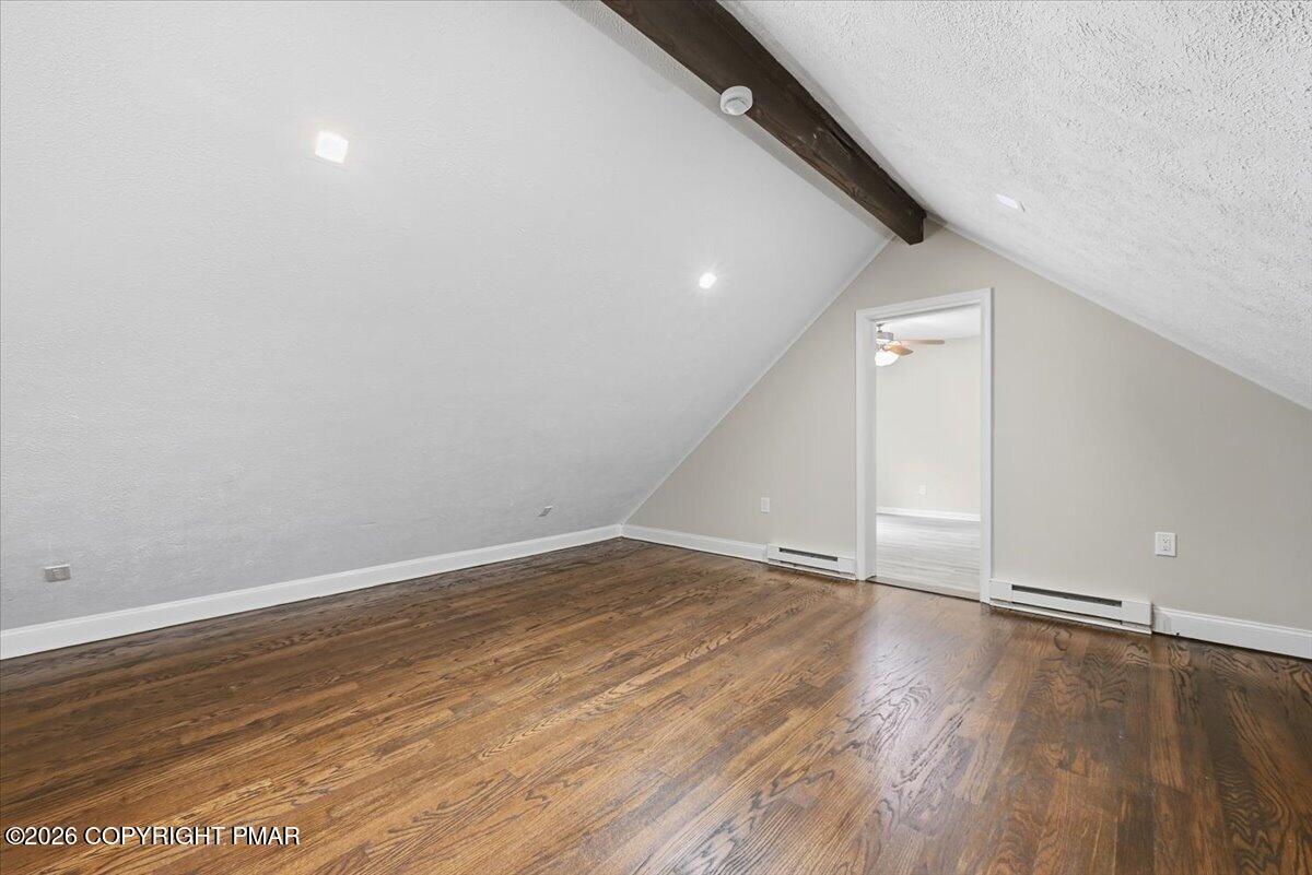 Finished attic room with sloped ceilings, an exposed beam, and hardwood floors.
