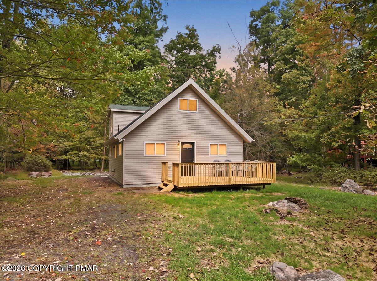 Gray gable-roofed house with a wooden deck nestled among autumn trees.