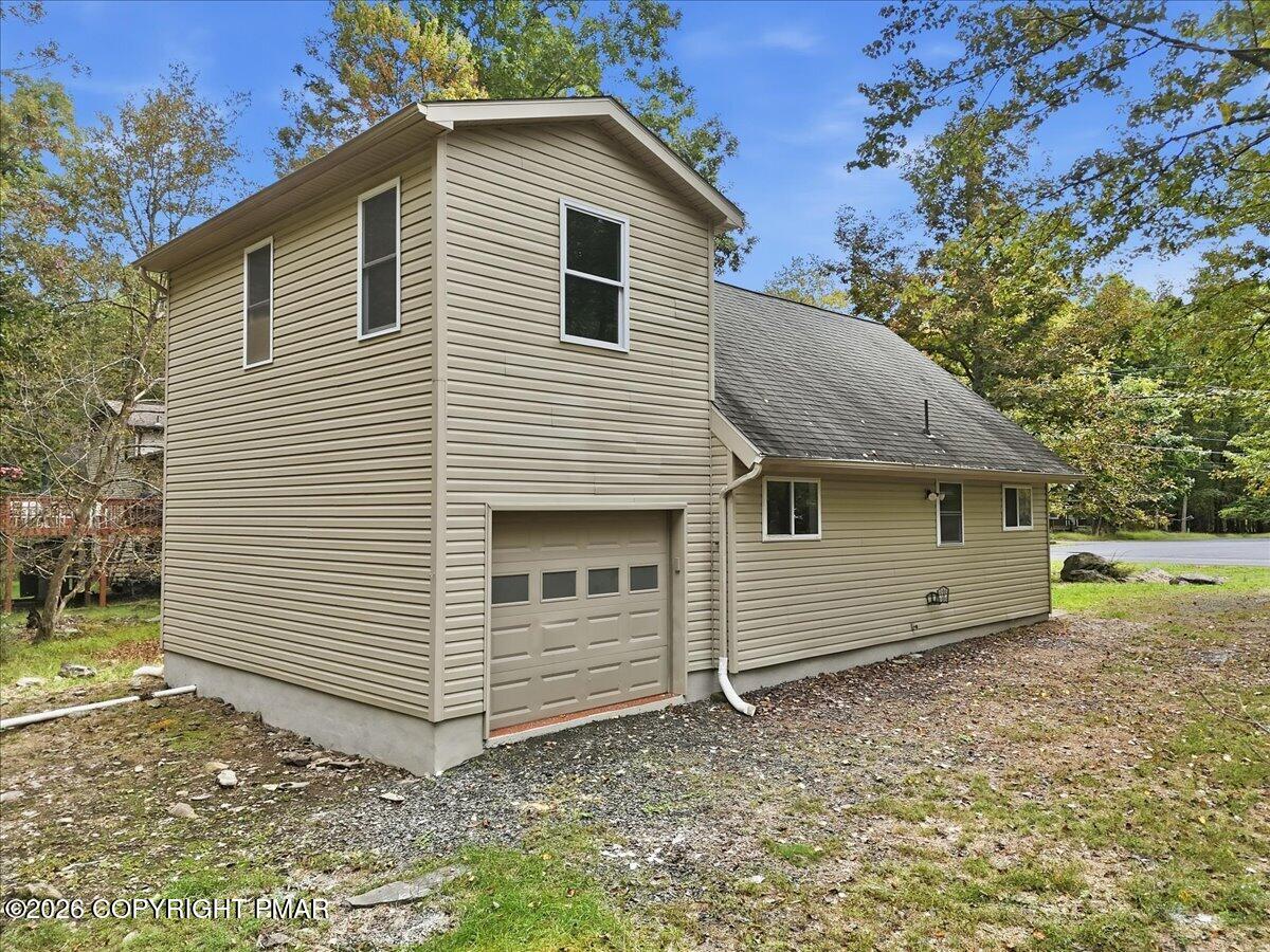 Beige-sided house with an attached garage, tall two-story section, and mature trees.