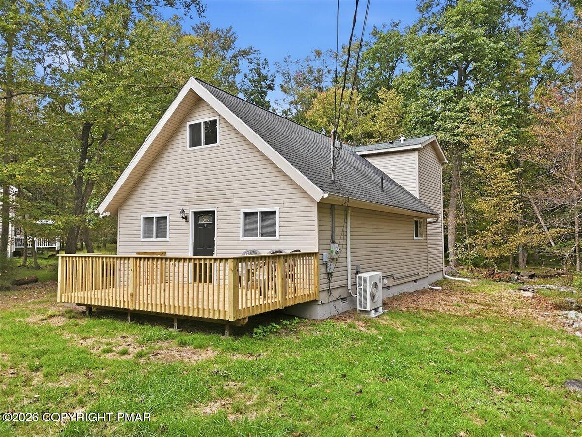 Beige gabled house with a raised wooden deck, surrounded by trees with autumn foliage.
