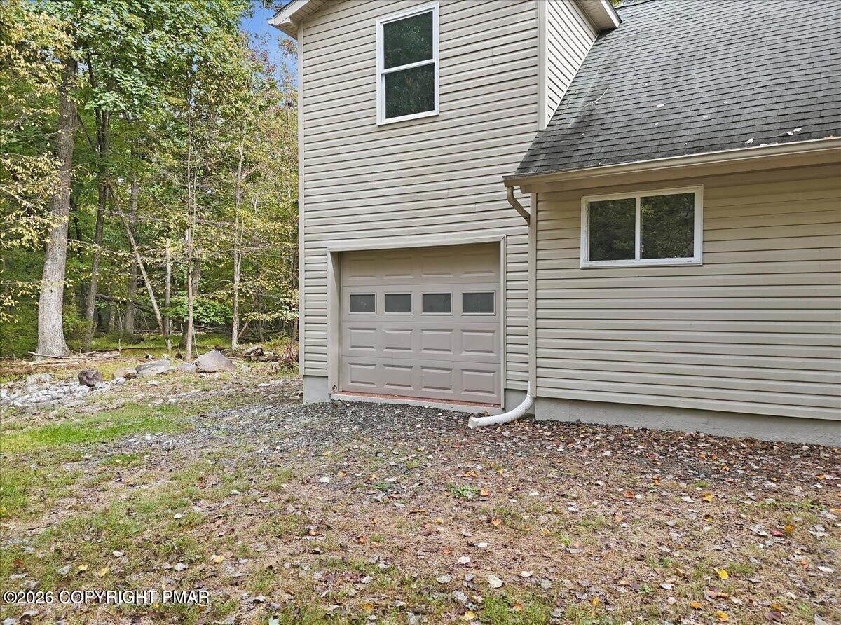 House exterior with a single-car garage beside a wooded, leaf-strewn yard.