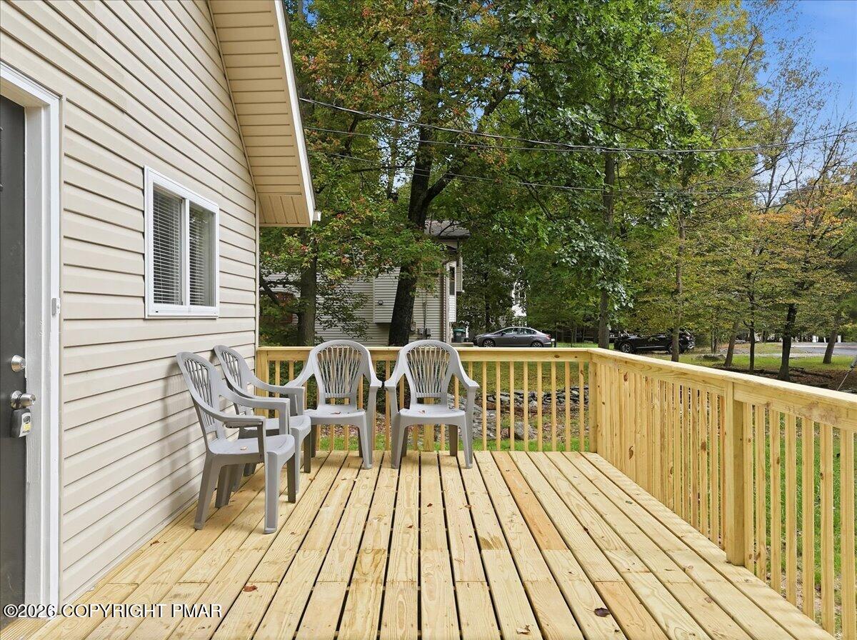 Wood deck beside a beige-sided home, furnished with gray chairs and overlooking a tree-filled yard.