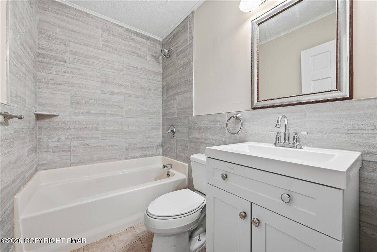 Bathroom with a gray-tiled tub and shower, white vanity, and framed mirror.