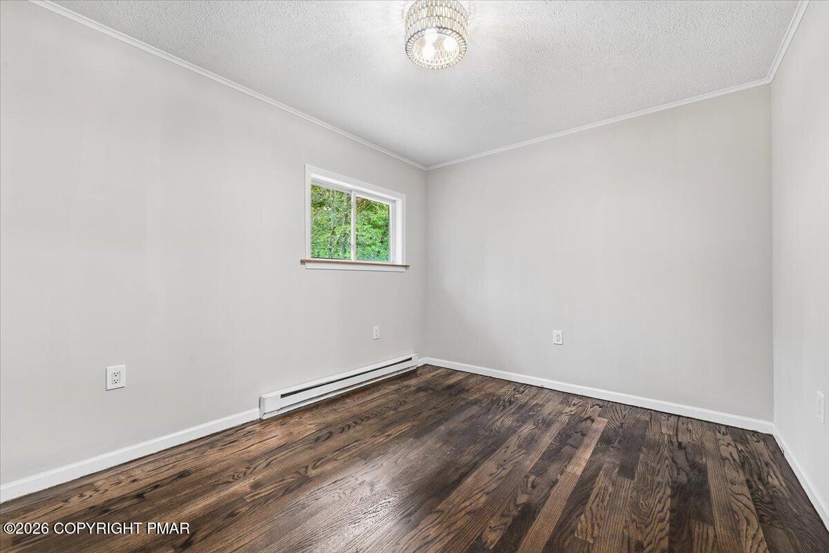 Empty room with dark hardwood floors, a small window, and a baseboard heater.