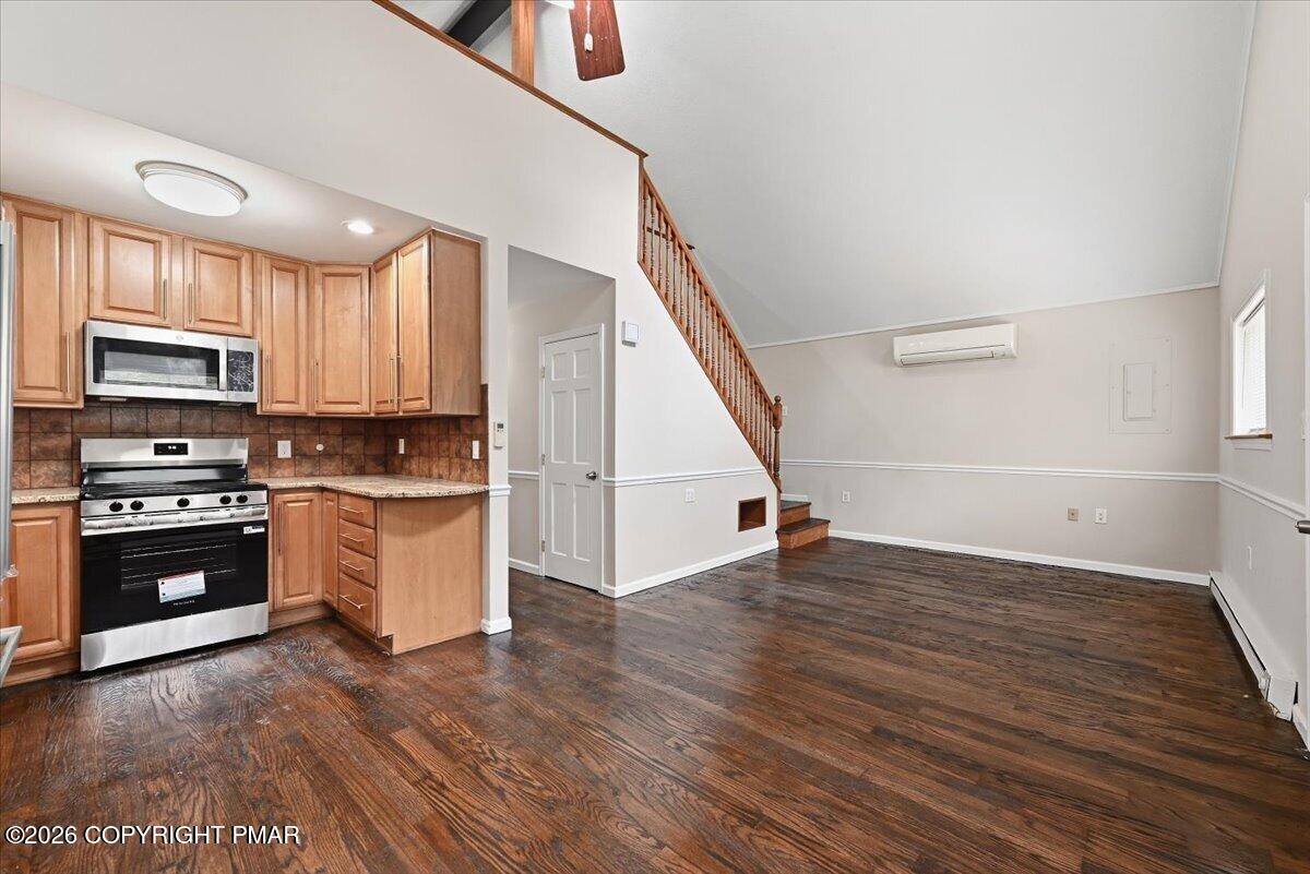 Open kitchen and living area with wood cabinets, stainless steel appliances, dark flooring, and a staircase.