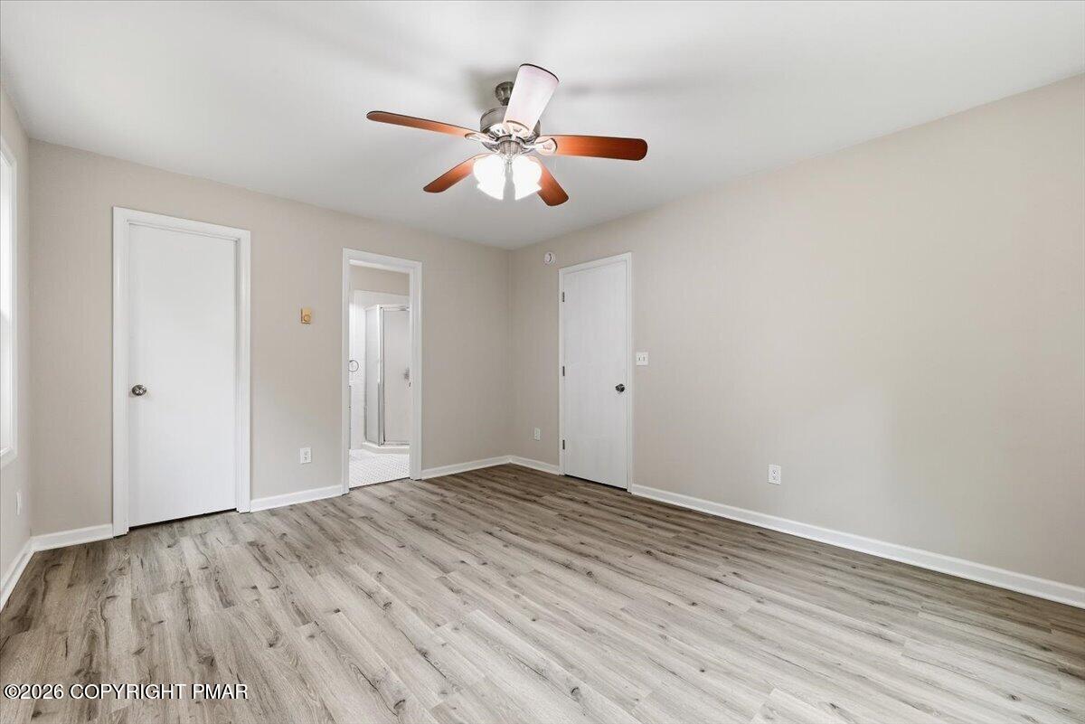 Empty bedroom with gray wood-look flooring, a ceiling fan, and an open doorway to a bathroom.