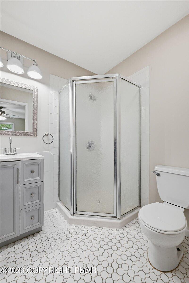 Bathroom with a corner glass shower, gray vanity, and white hexagonal tile floor.