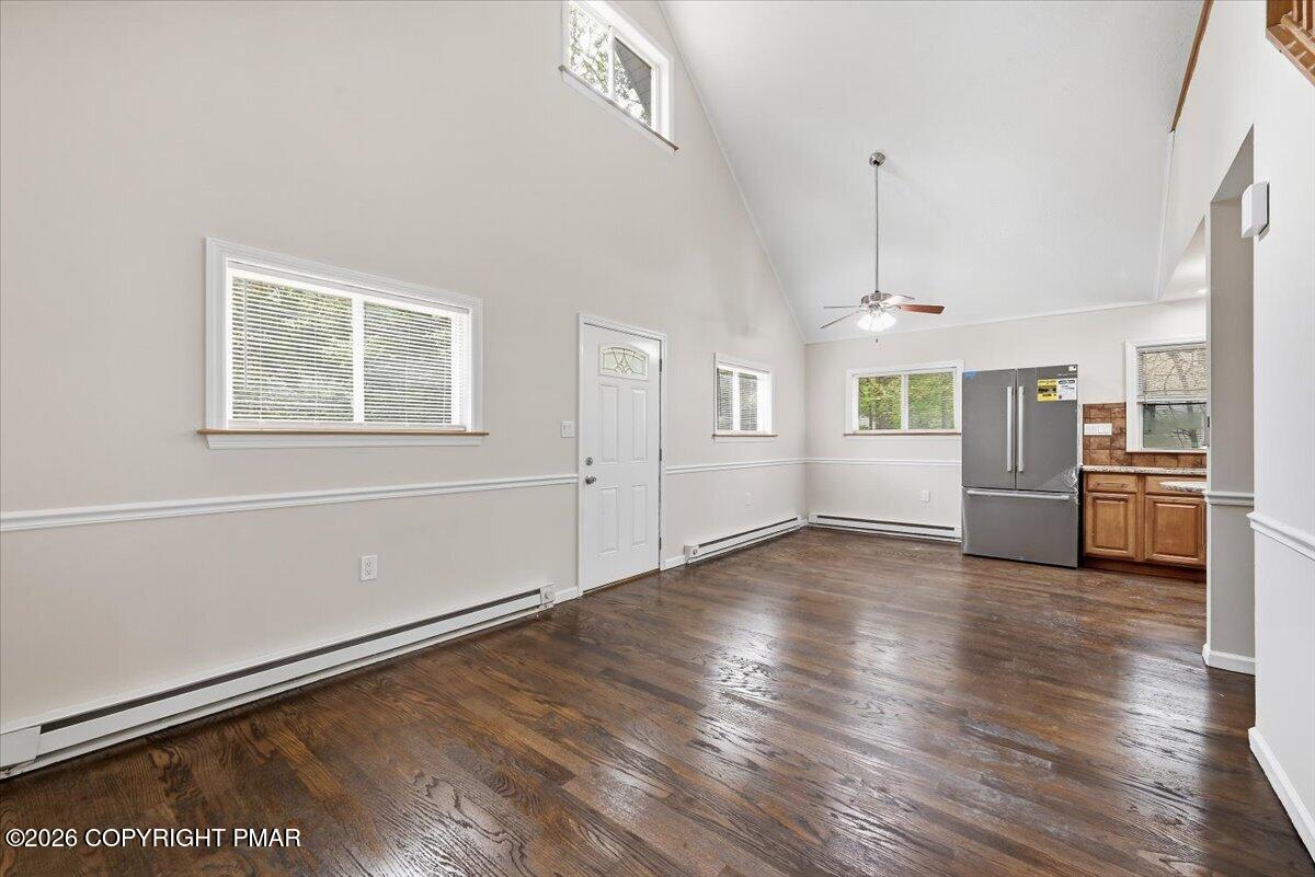 Open living area with dark hardwood floors, vaulted ceiling, and kitchen at the back.