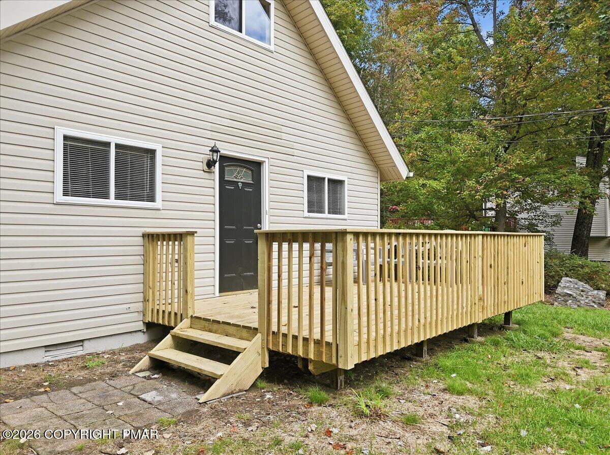 Light-sided house with a raised wooden deck, railings, and steps beside mature trees.