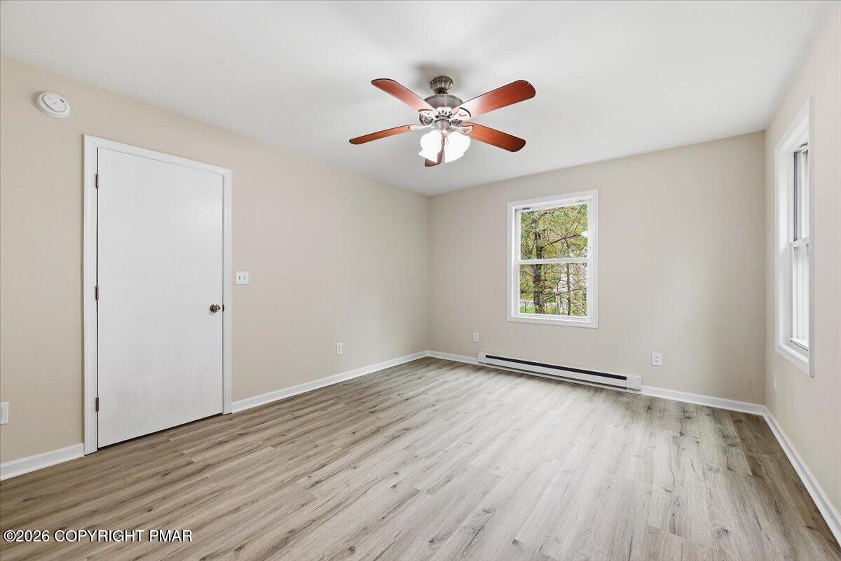 Empty room with light wood-look flooring, a ceiling fan, and two windows.