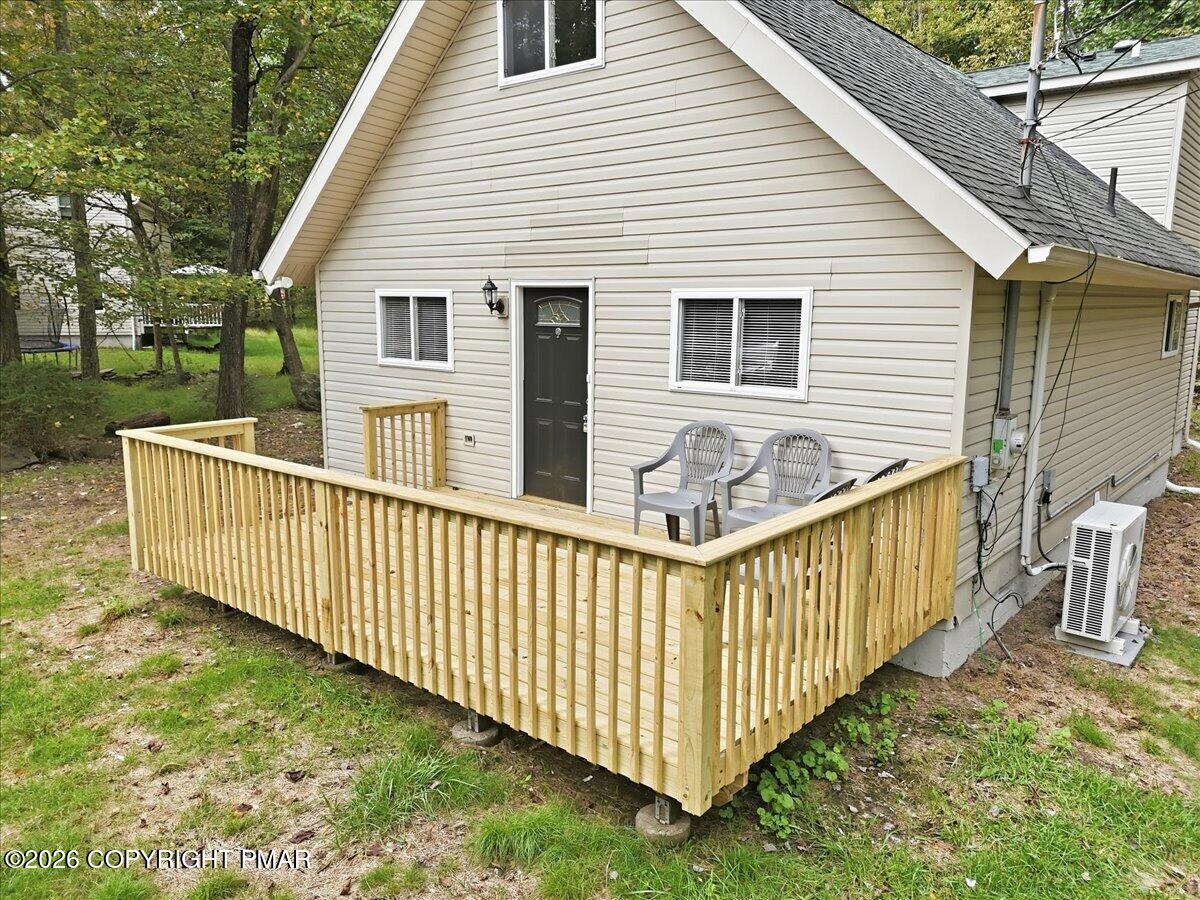 Light-sided home with a raised wooden deck, patio chairs, and a dark front door.
