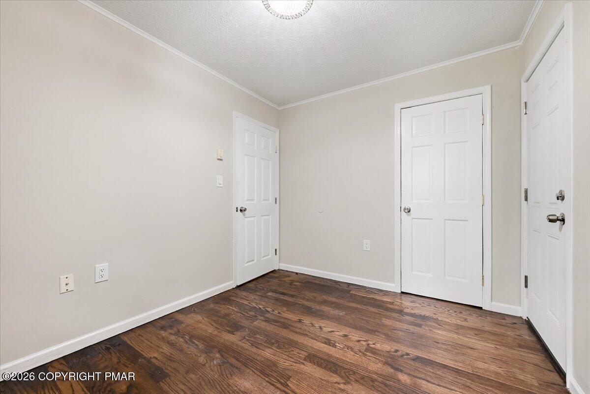 Empty room with dark hardwood floors, beige walls, and three white paneled doors.