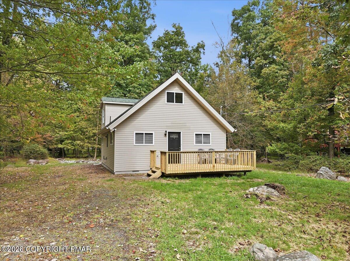 Beige gabled house with a wooden front deck surrounded by trees.