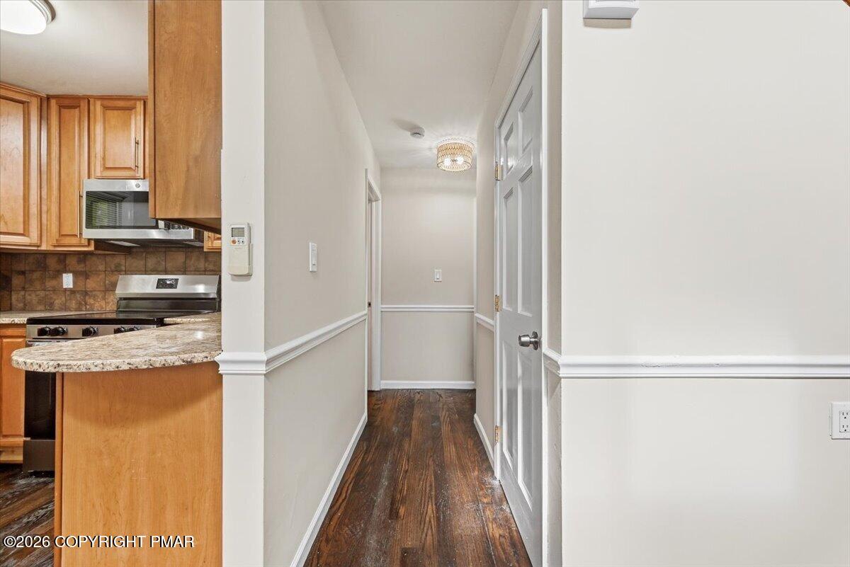 Hallway with dark wood floors beside a kitchen with wood cabinets and a granite breakfast bar.