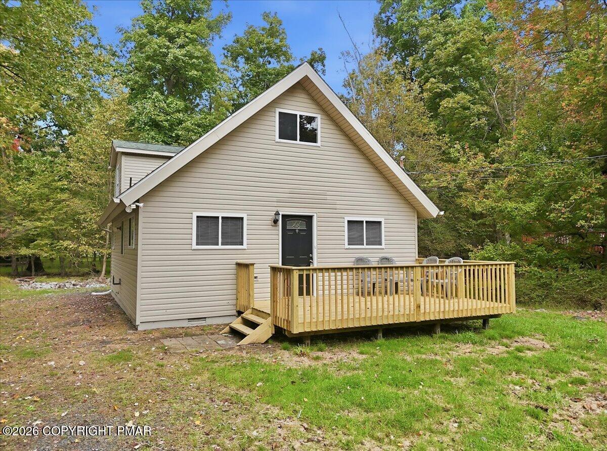 Beige gabled house with a raised wooden deck in a wooded yard.