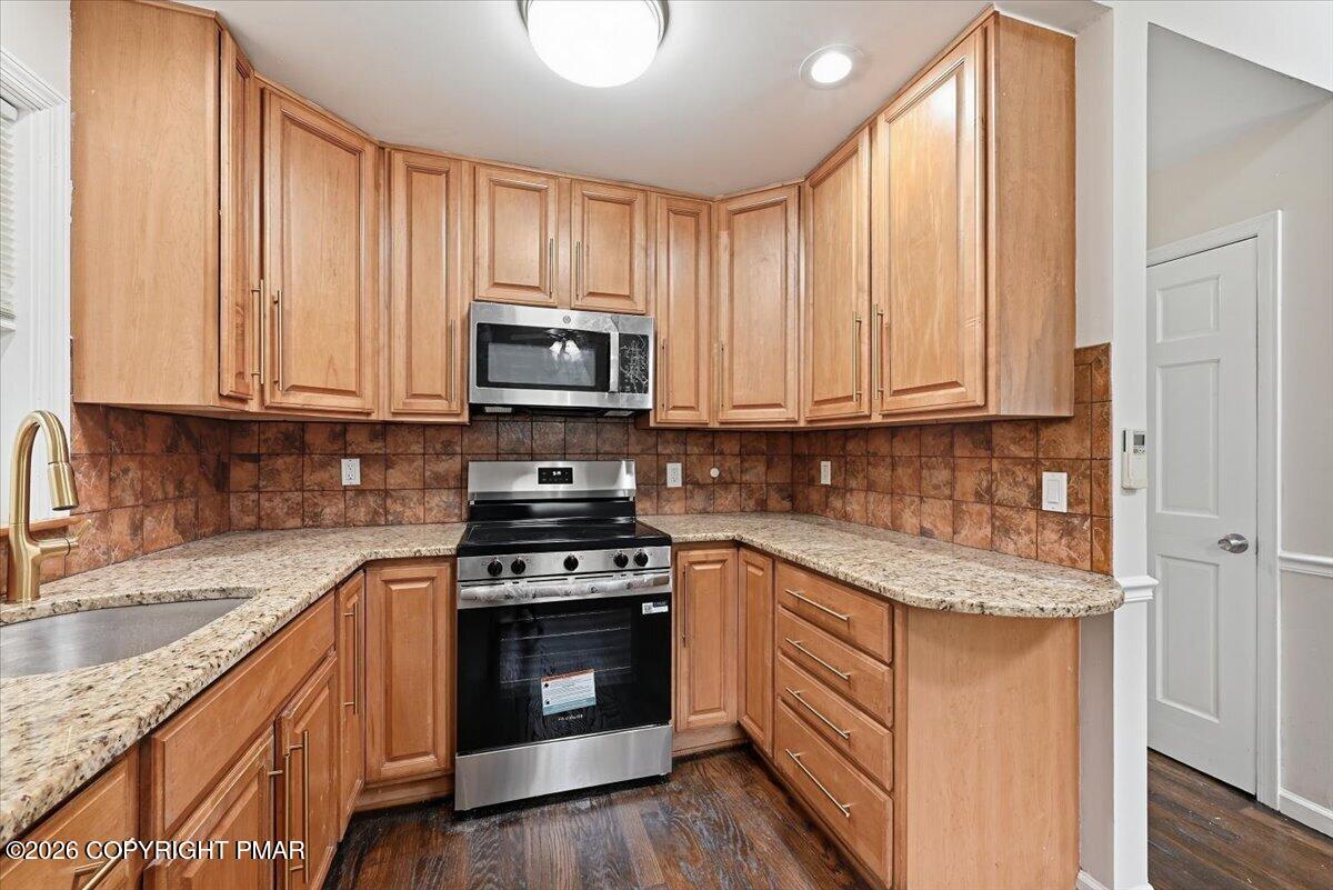 Kitchen with warm wood cabinetry, granite counters, and a stainless steel range and microwave.