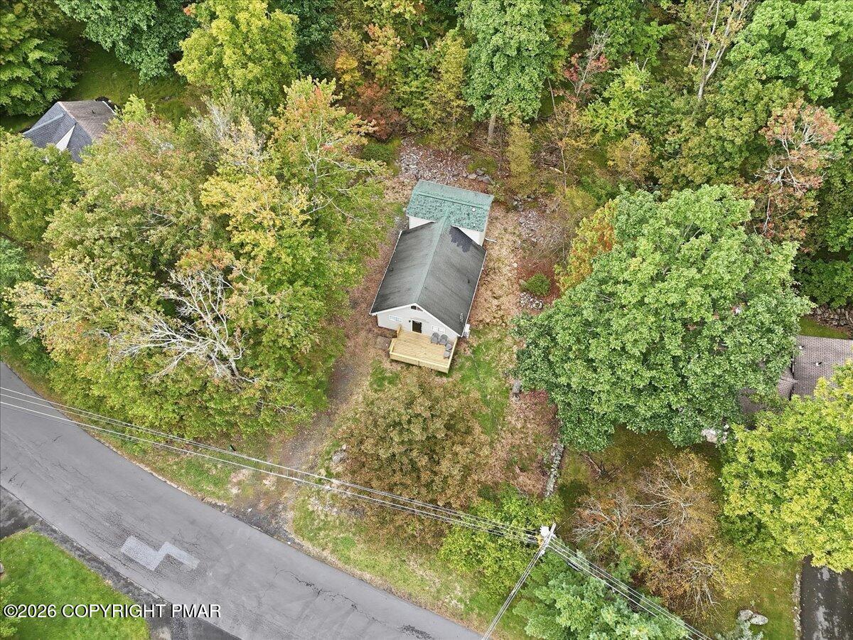 Aerial view of a house and wooden deck surrounded by dense trees beside a road.