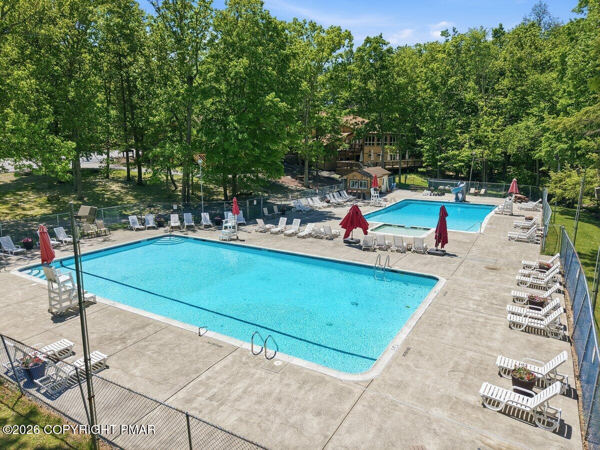 Outdoor pool complex with two swimming pools, lounge chairs, and surrounding trees.
