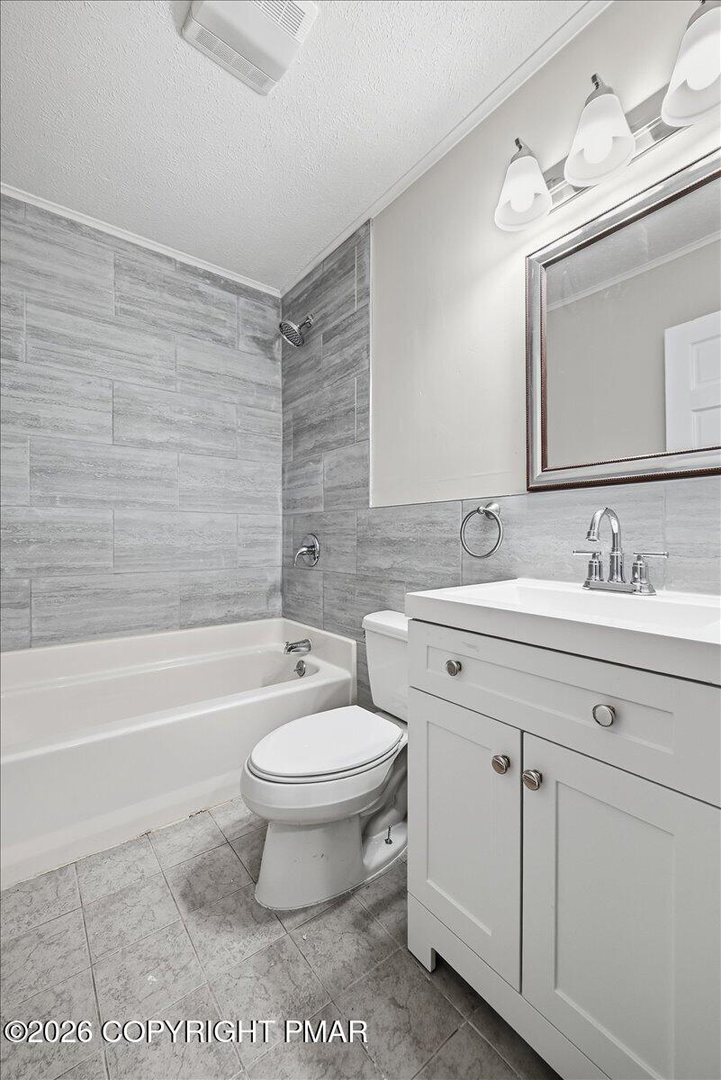 Bathroom with gray tile, a white tub and shower, toilet, and vanity.