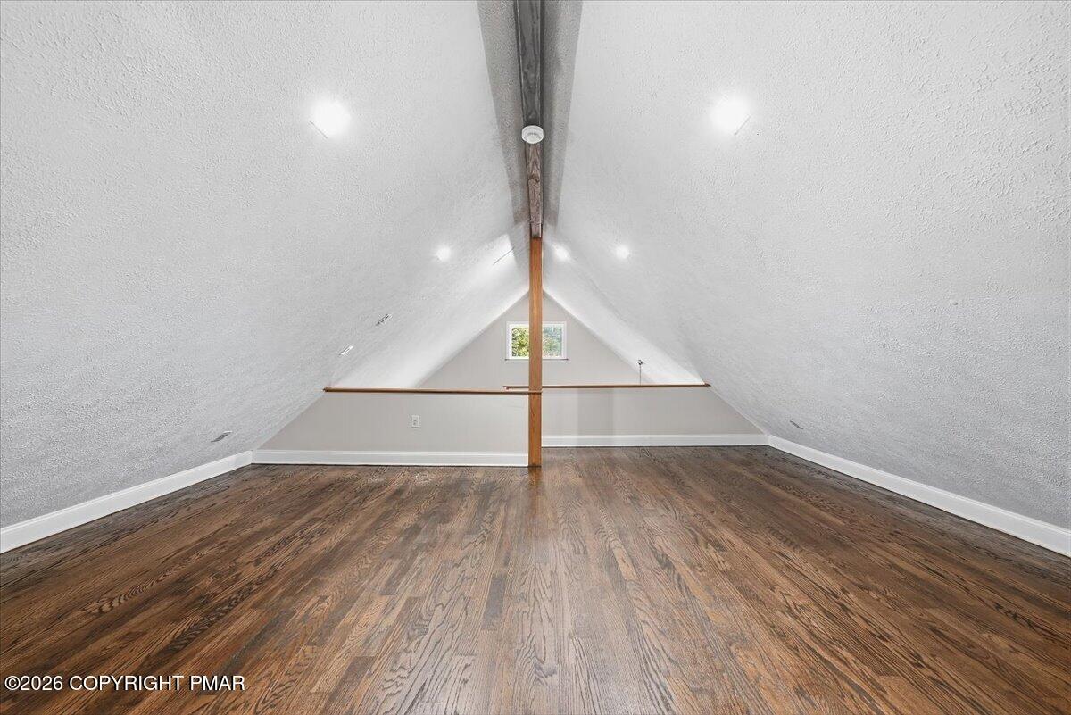 Unfurnished attic loft with sloped ceilings, exposed wooden beams, and dark hardwood floors.