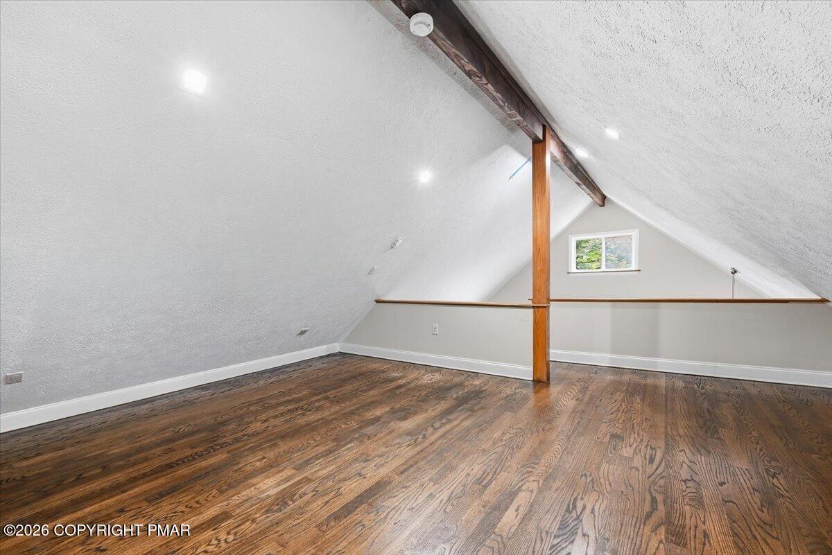 Finished loft with vaulted ceilings, exposed wooden beams, and dark wood flooring.