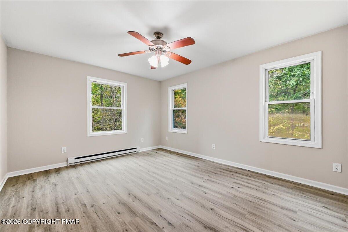 Empty bedroom with gray wood-look flooring, three windows, and a ceiling fan.