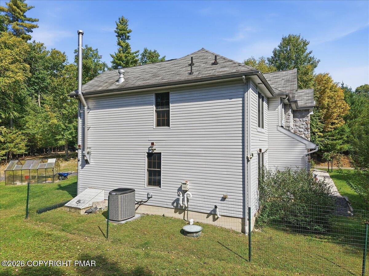 Side of a gray-sided house with a fenced yard, greenhouse, and stone chimney.