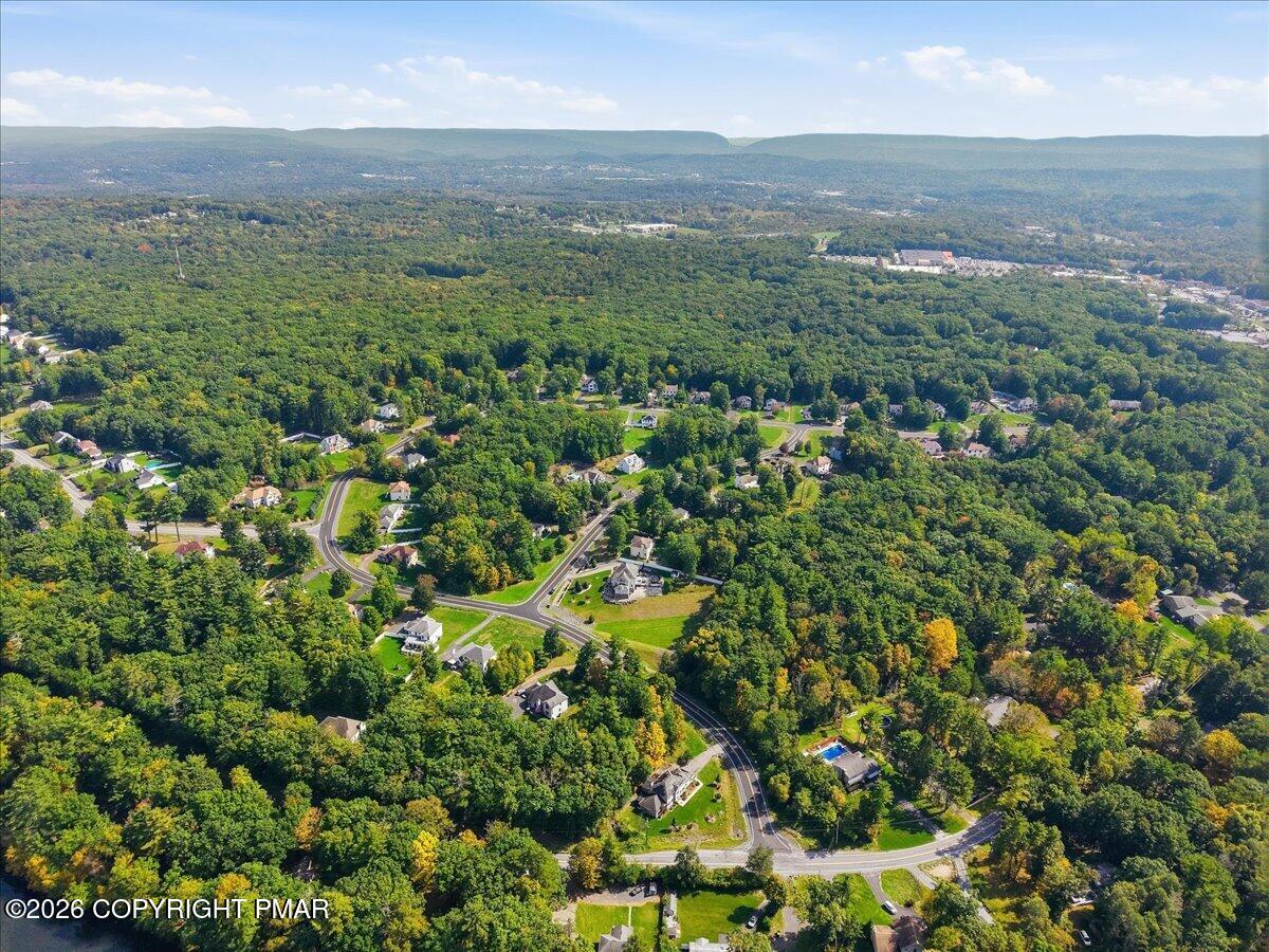 Aerial view of wooded homes and winding roads with a mountain ridge in the distance.