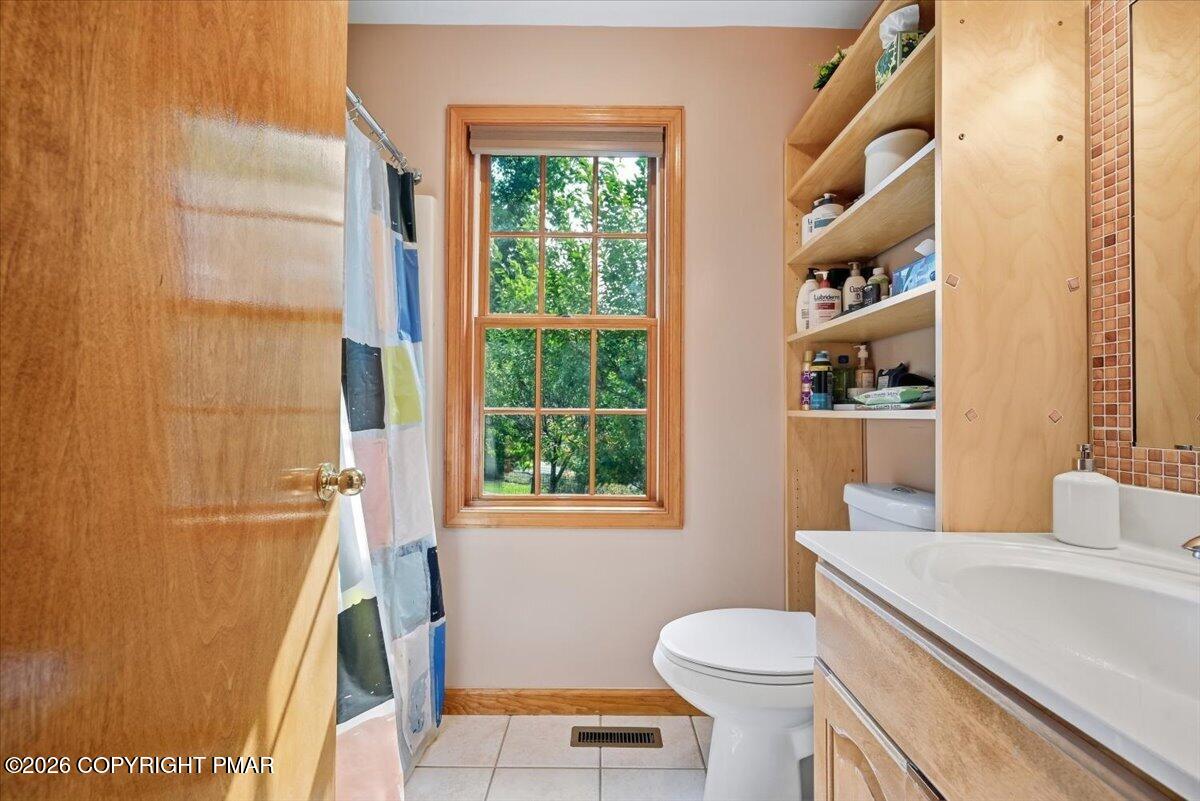 Bathroom with a tiled shower, wood vanity and shelving, and a large window overlooking trees.