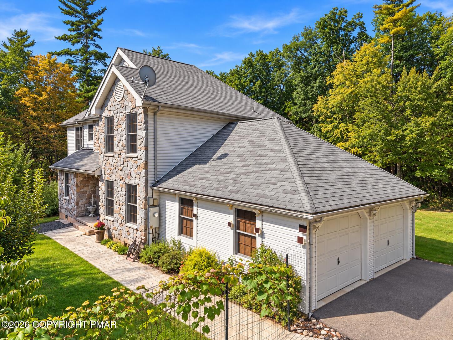 Two-story home with a stone facade, white siding, attached garage, and autumn trees.