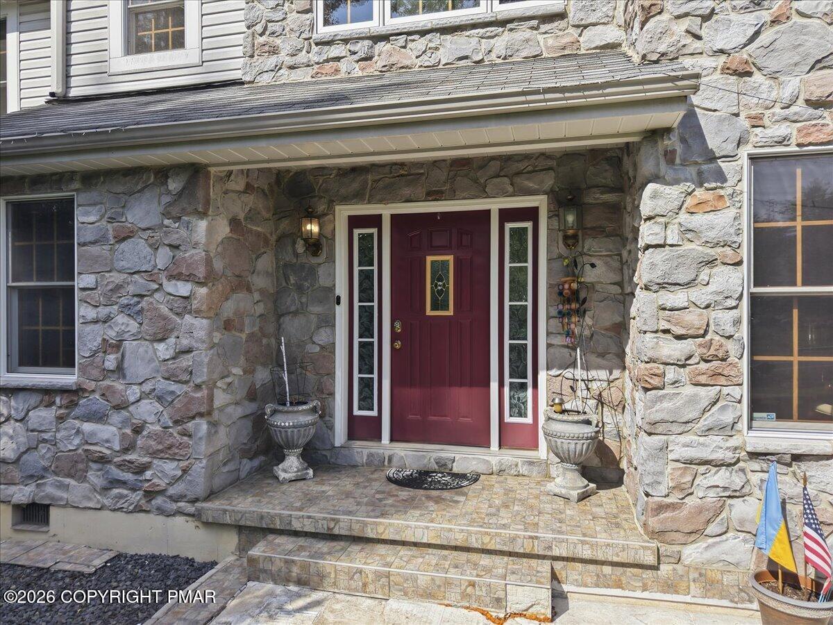 Stone home entrance with a burgundy door, glass sidelights, tiled steps, and urn planters.