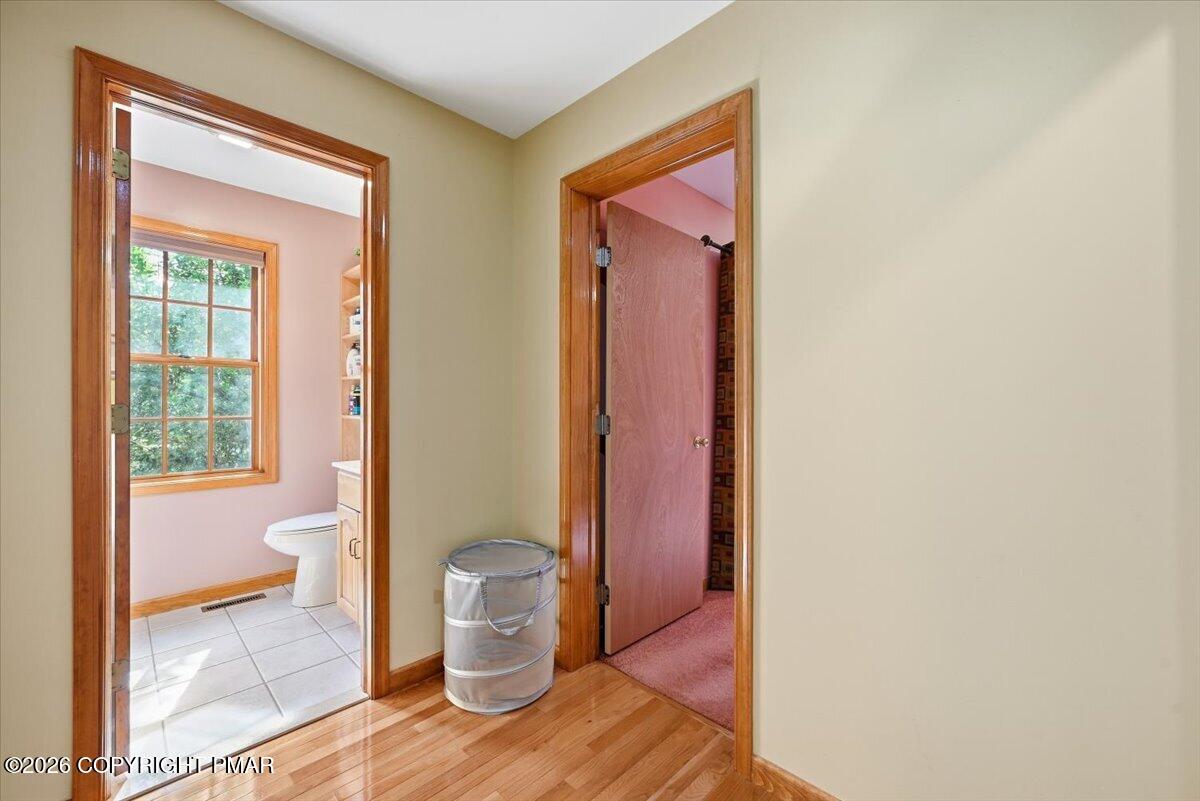 Hallway with hardwood floors and wood-trimmed doorways to a bright bathroom and carpeted room.