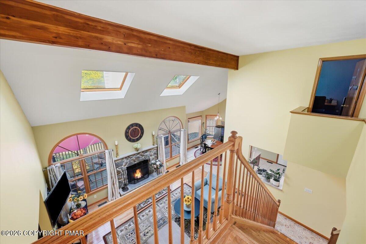 Open living room with stone fireplace, vaulted ceiling, skylights, and a wood staircase railing.
