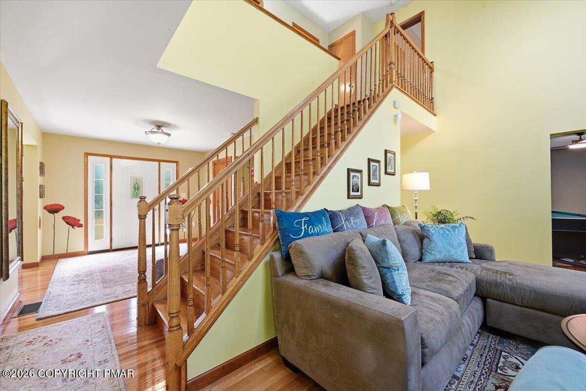 Living room with a gray sectional beside a wooden staircase and hardwood-floored entry hall.