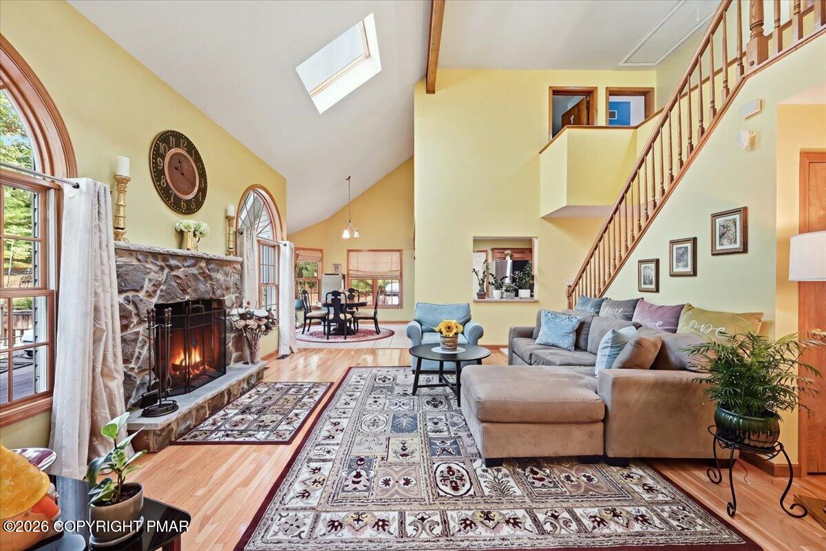 Vaulted living room with a stone fireplace, arched windows, skylight, and open staircase.