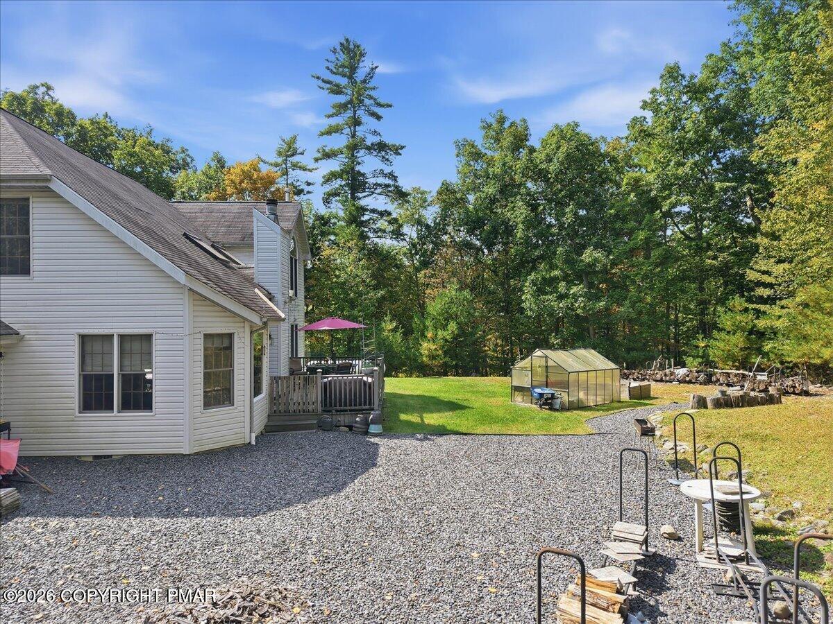 Home beside a gravel backyard with a deck, patio seating, and a greenhouse.