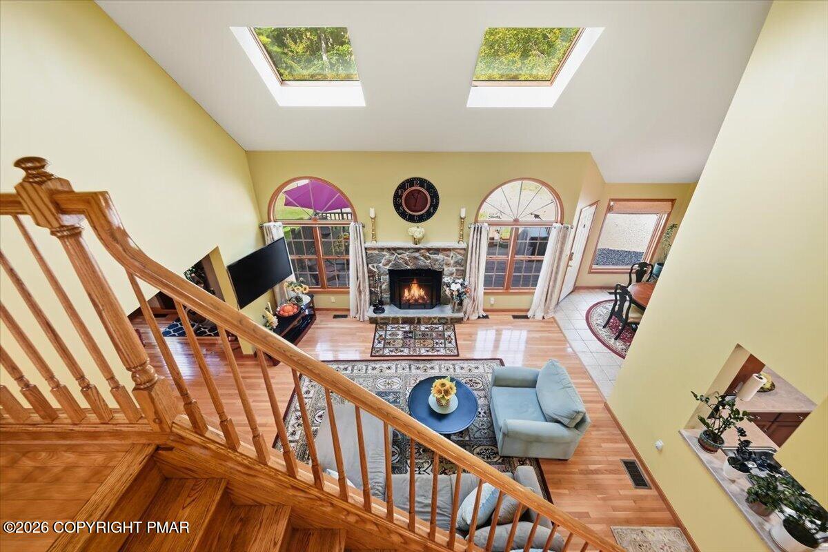 Living room with a stone fireplace, arched windows, and skylights, viewed from the staircase.