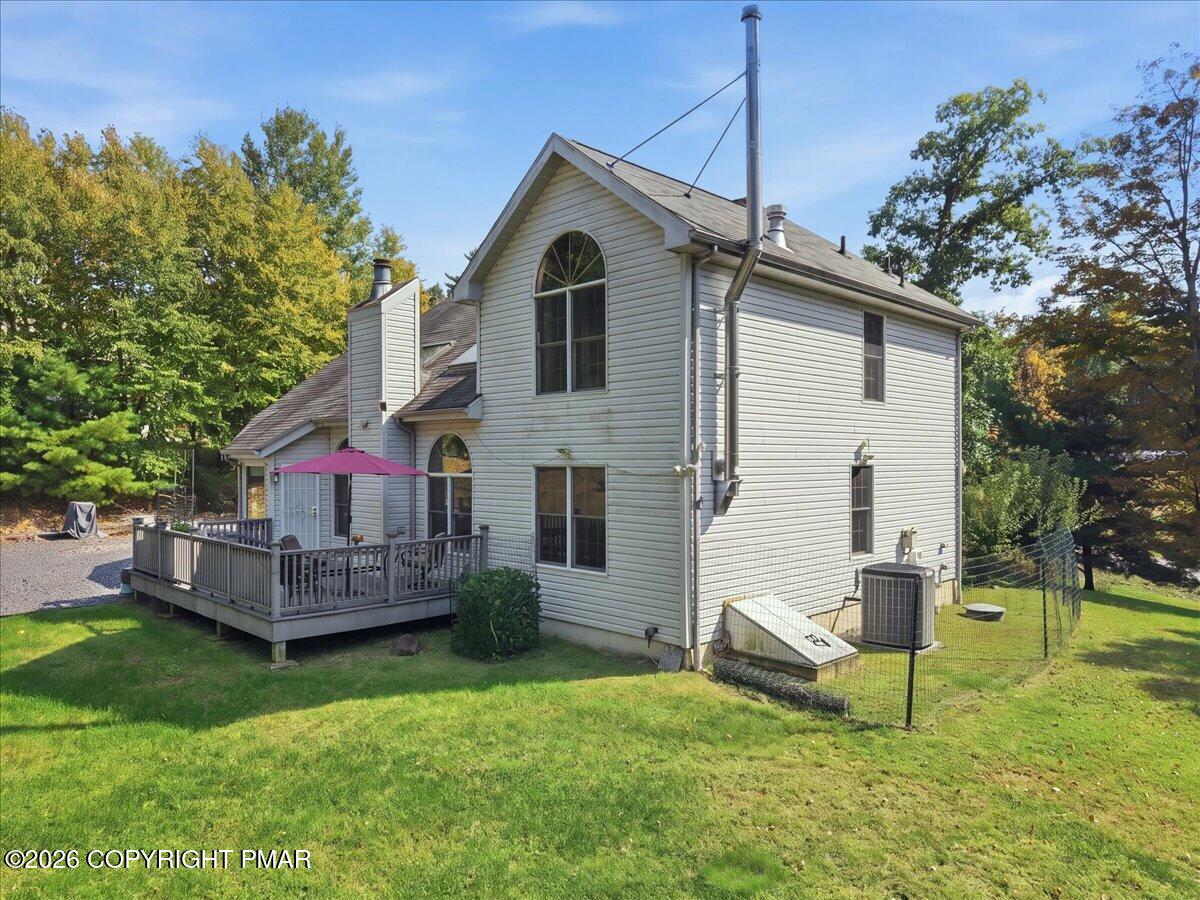 Rear of a two-story home with a raised deck, pink umbrella, and tall arched window.