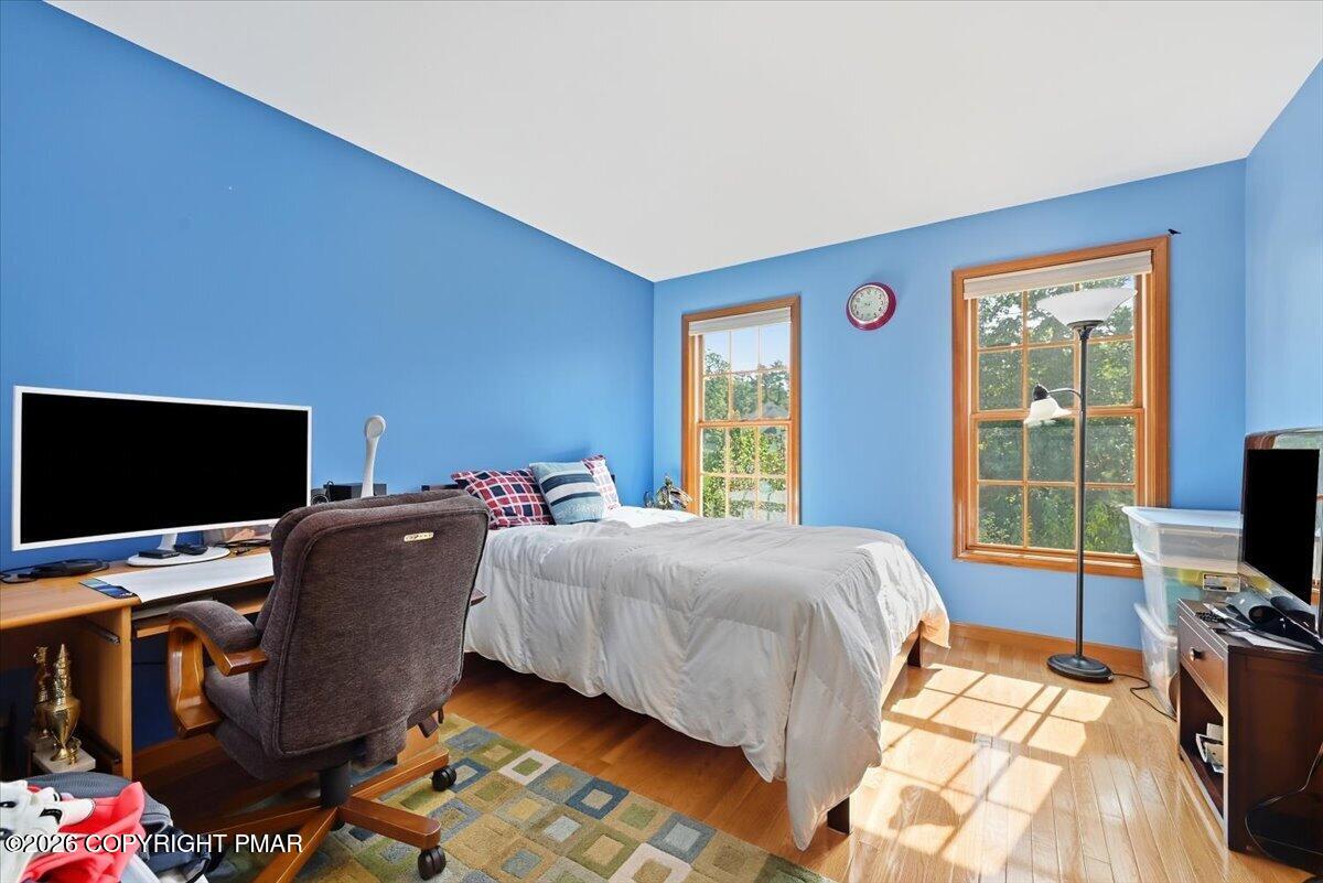 Bedroom with blue walls, a bed, desk, and sunlit hardwood floor.