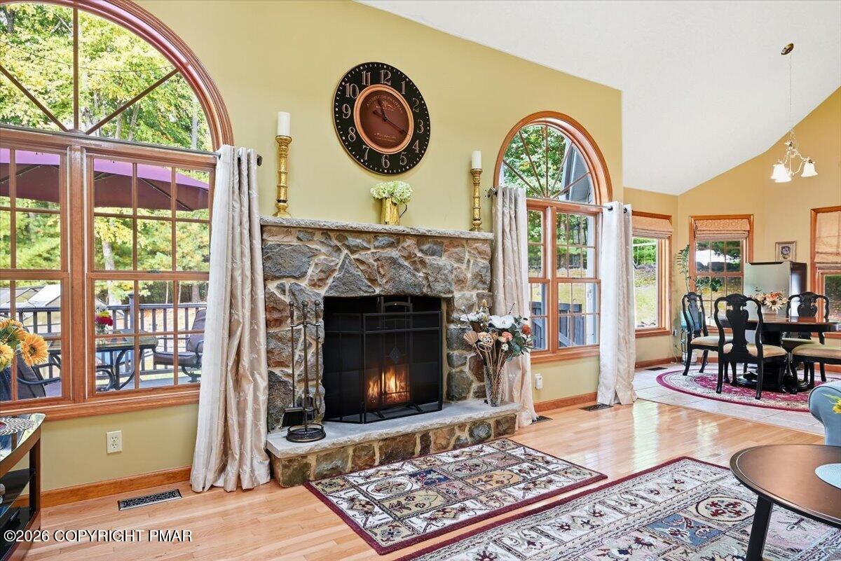 Living room with a stone fireplace, tall arched windows, hardwood floors, and an adjoining dining area.