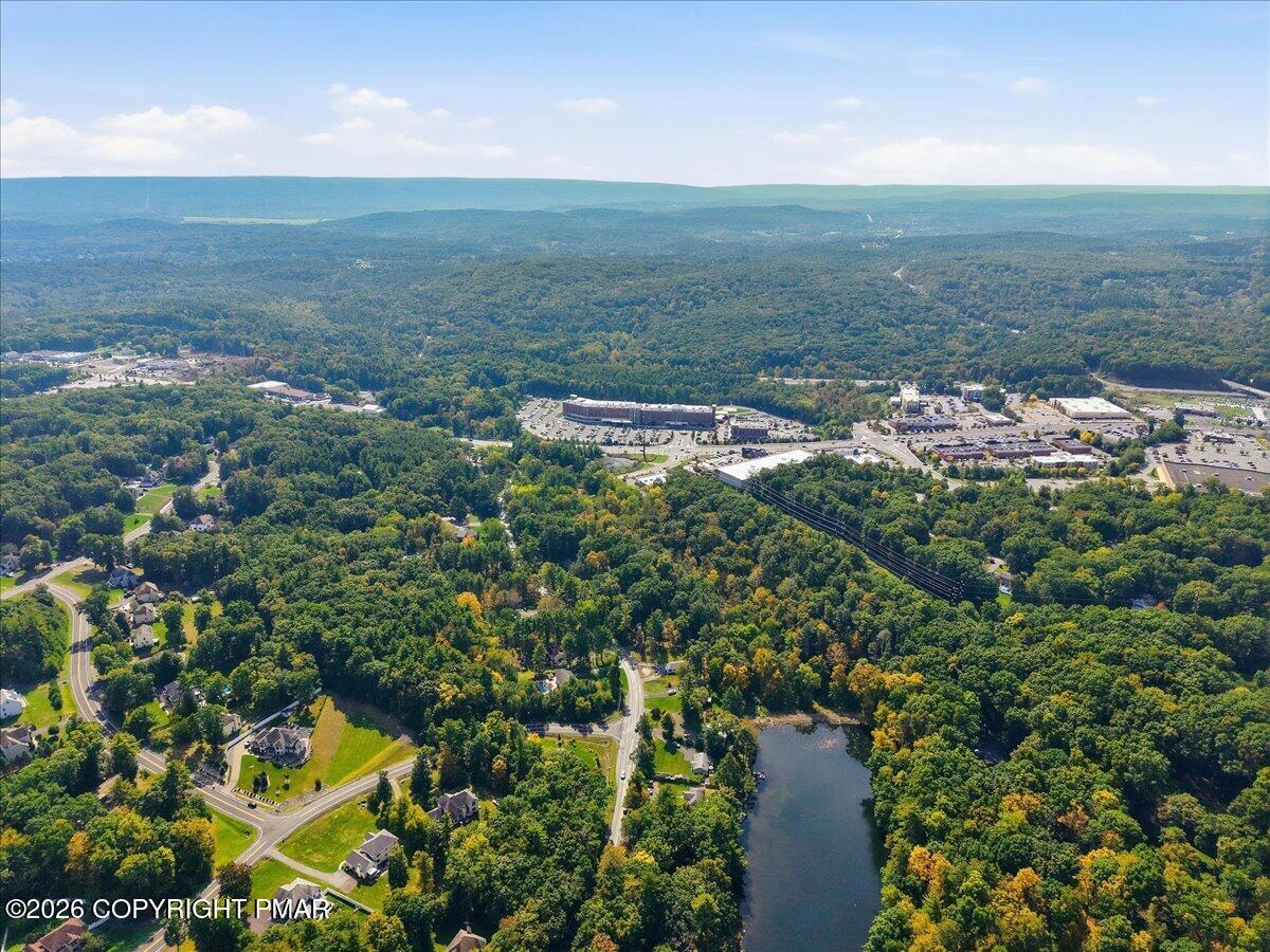 Aerial view of wooded homes and shopping district, with water in the foreground and distant ridgelines.