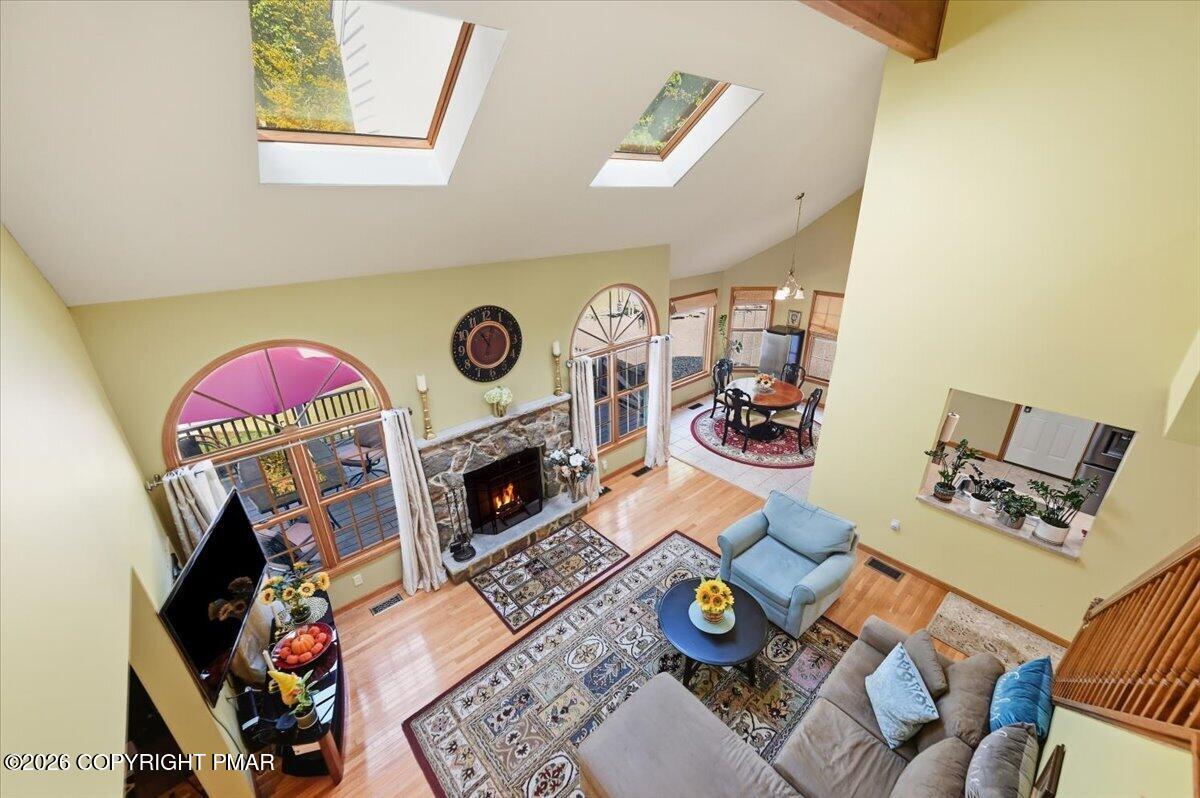 Living room with vaulted skylit ceiling, stone fireplace, arched windows, and patterned rugs.